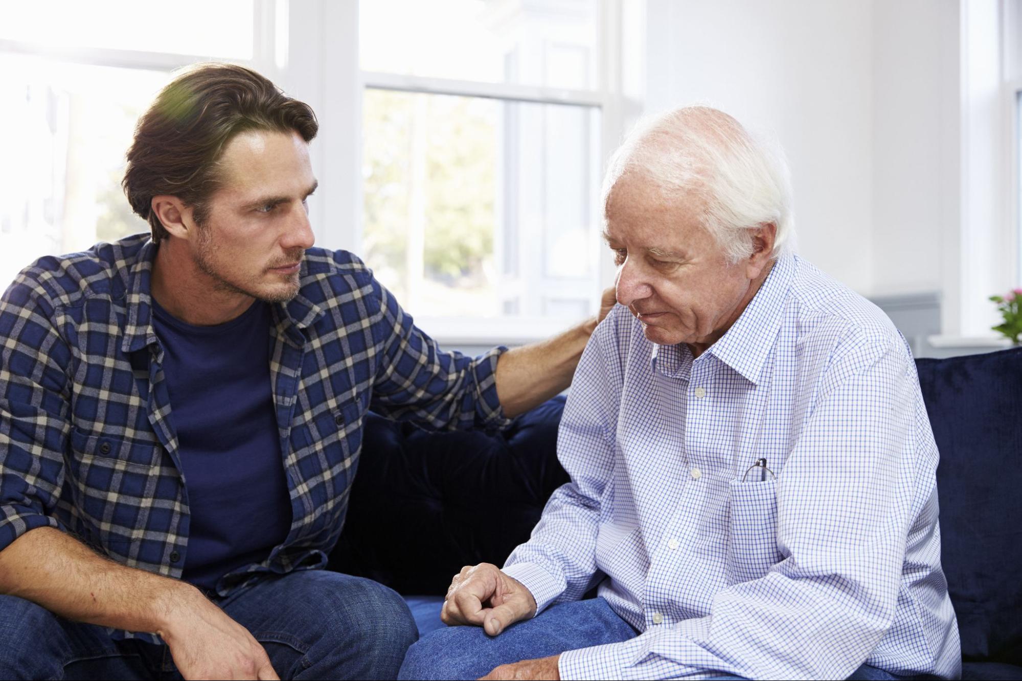 A middle-aged man comforting his senior father about his dementia.