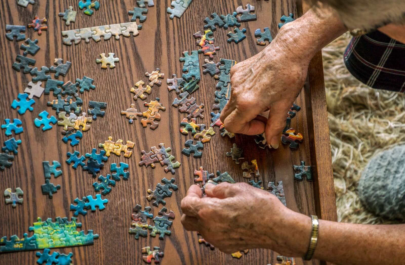 A top-down image of a senior assembling a puzzle.