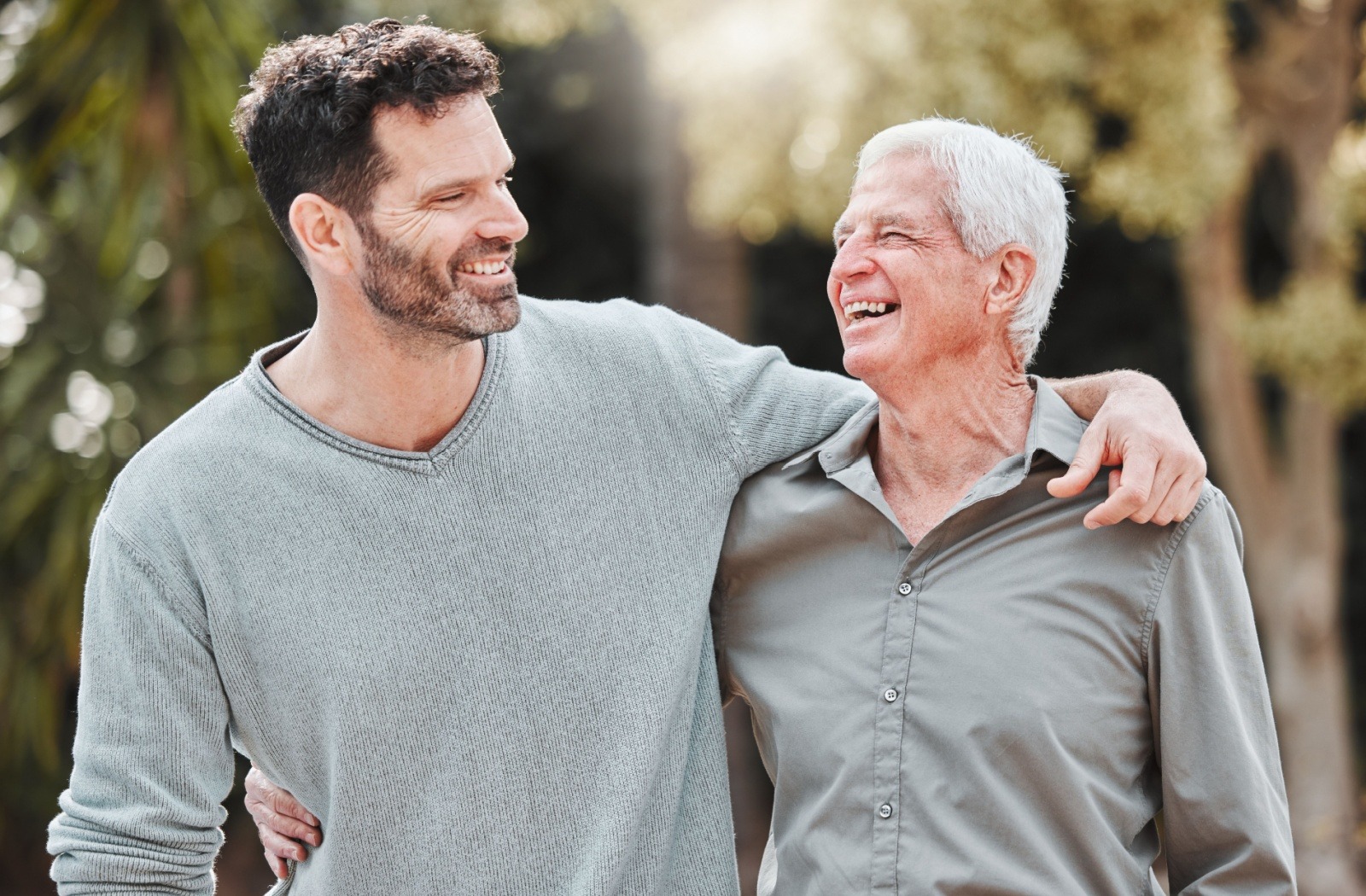 An adult child and their senior loved one laugh as they enjoy a walk together outdoors.
