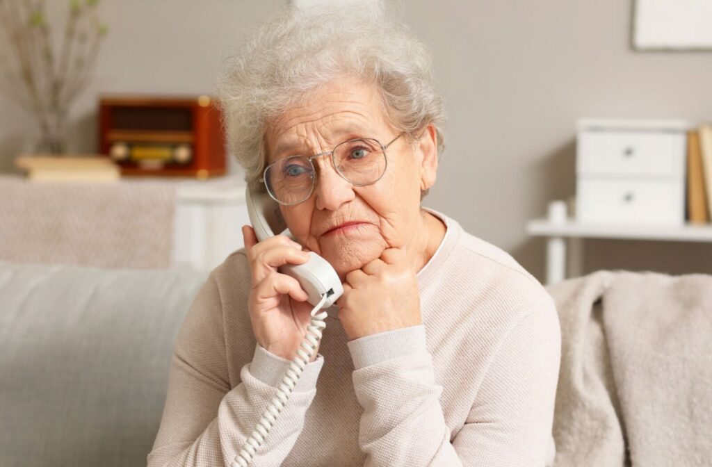 a senior sits on a couch speaking on a landline phone